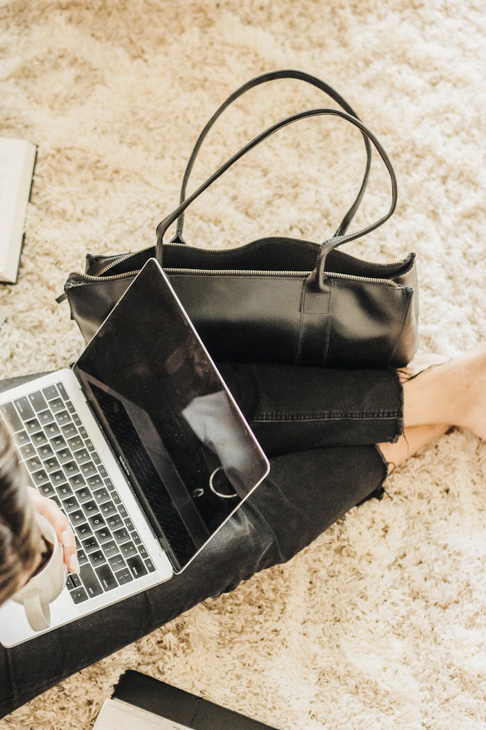 A stylish leather tote bag next to a laptop in a cozy indoor setting, ideal for modern travel.